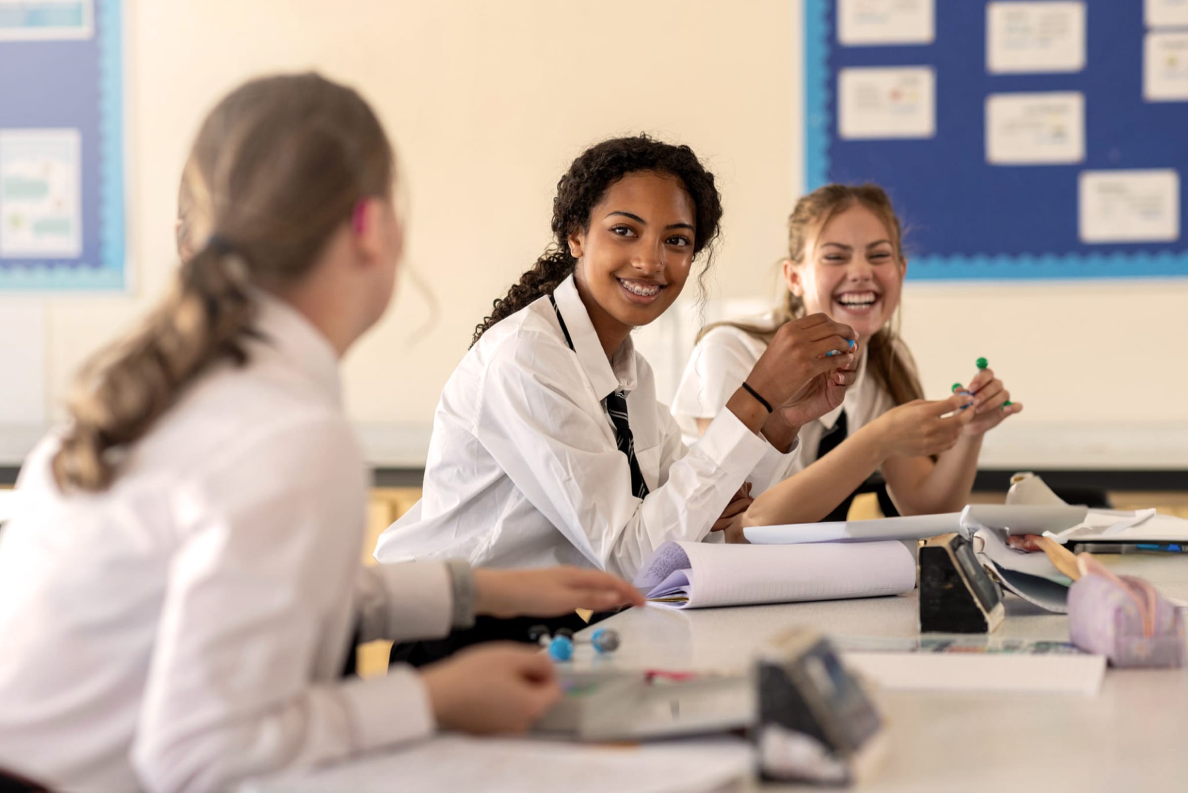 Smiling secondary pupils in white shirts and ties talk together around a classroom table