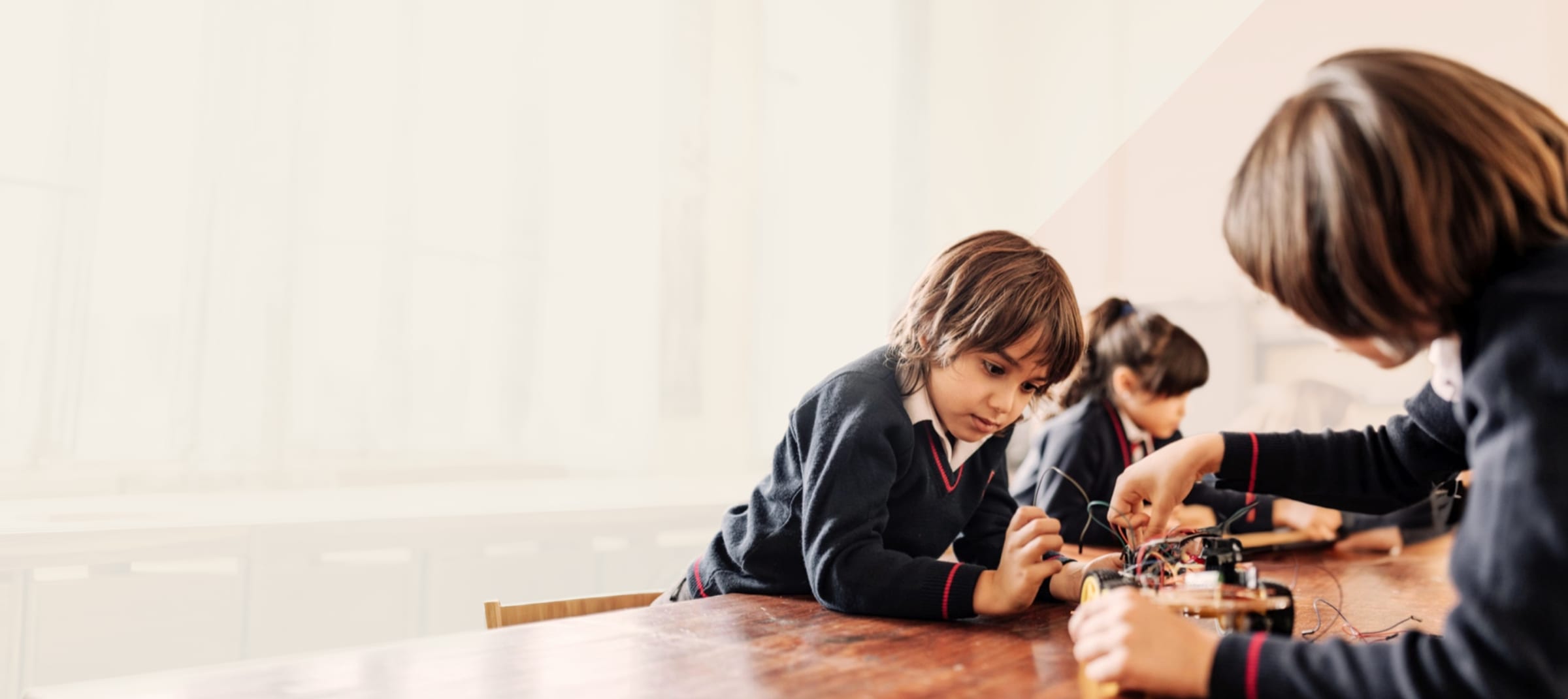 Young pupils in school uniform building and wiring a small robot car at a classroom table
