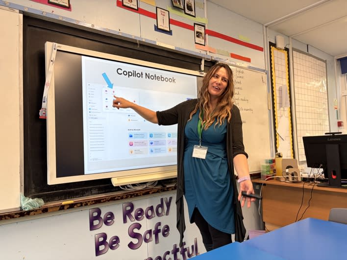 A trainer points to a Copilot Notebook screen at the front of a classroom during a staff training session