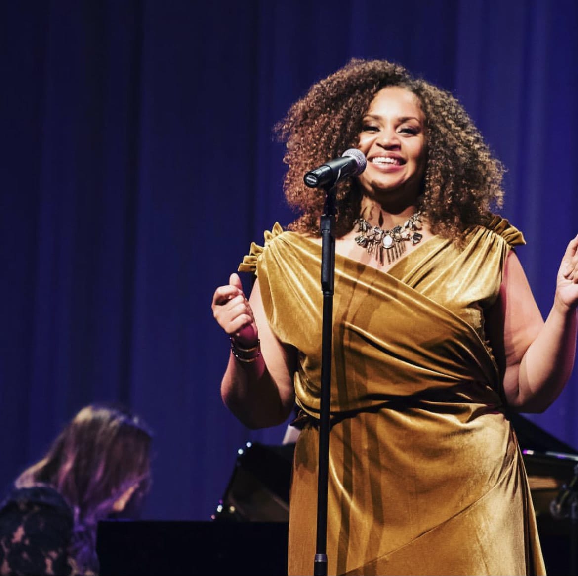 a smiling singer wearing gold dress at a microphone