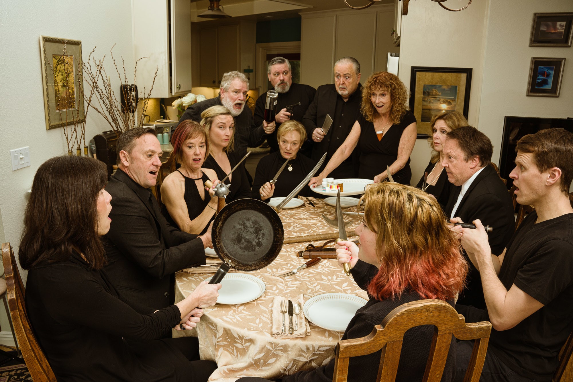 A large group of white men and women around a dinner table holding kitchen utensils as weapons