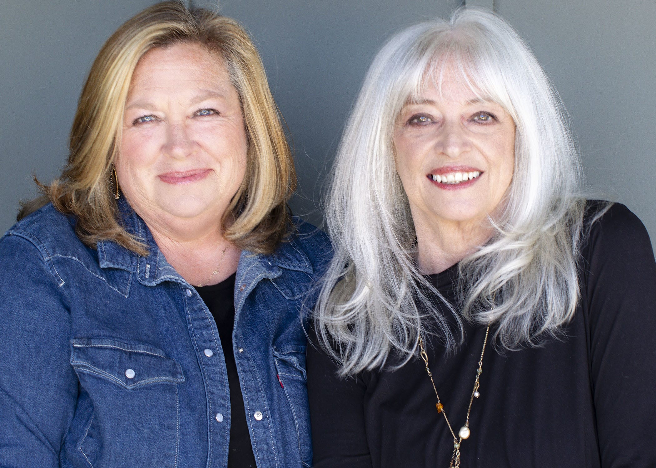 two white women one blonde and one with white hair sitting and smiling next to one another