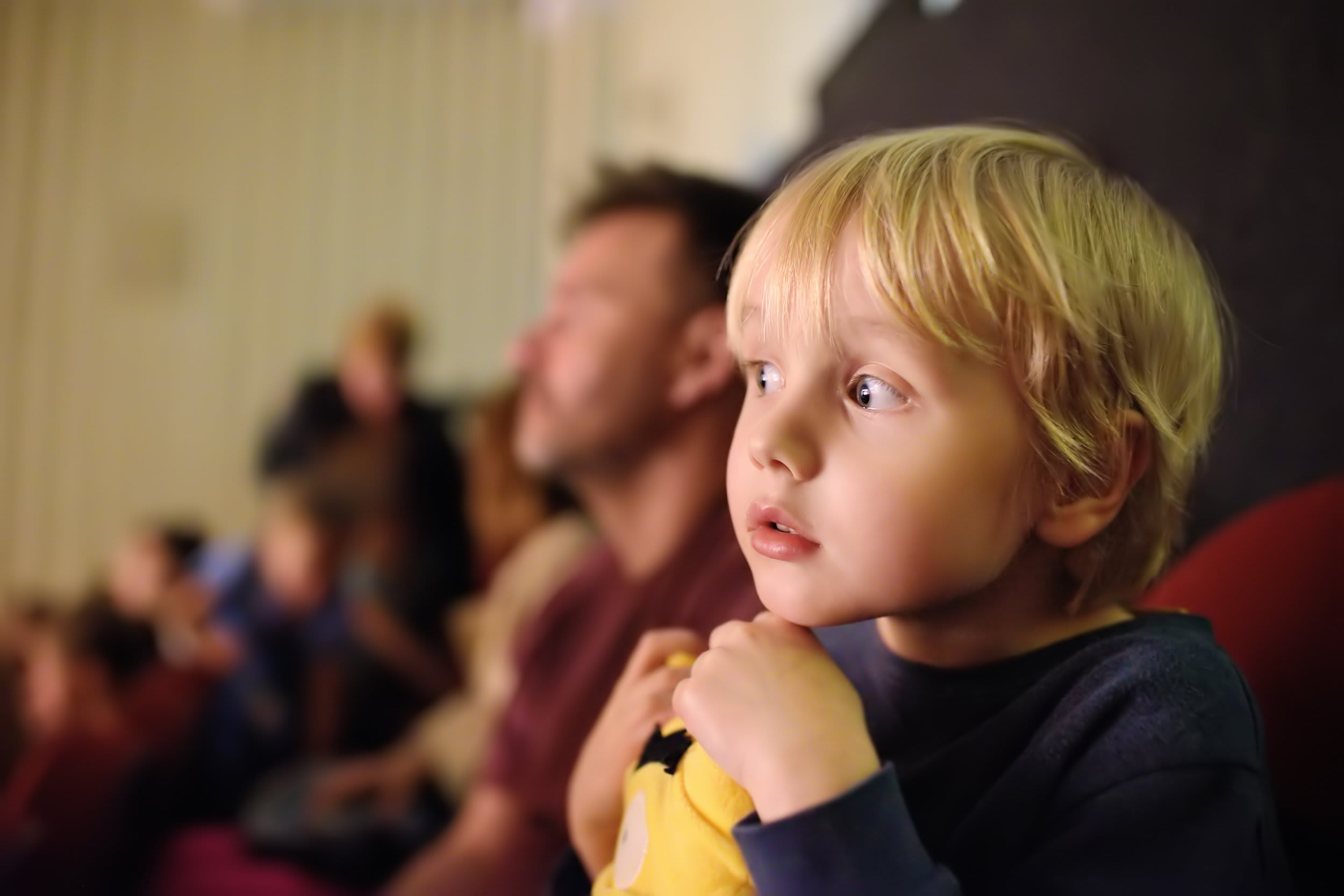 A cute young boy with his father are seated in a theatre. The young boy is obviously enthralled.