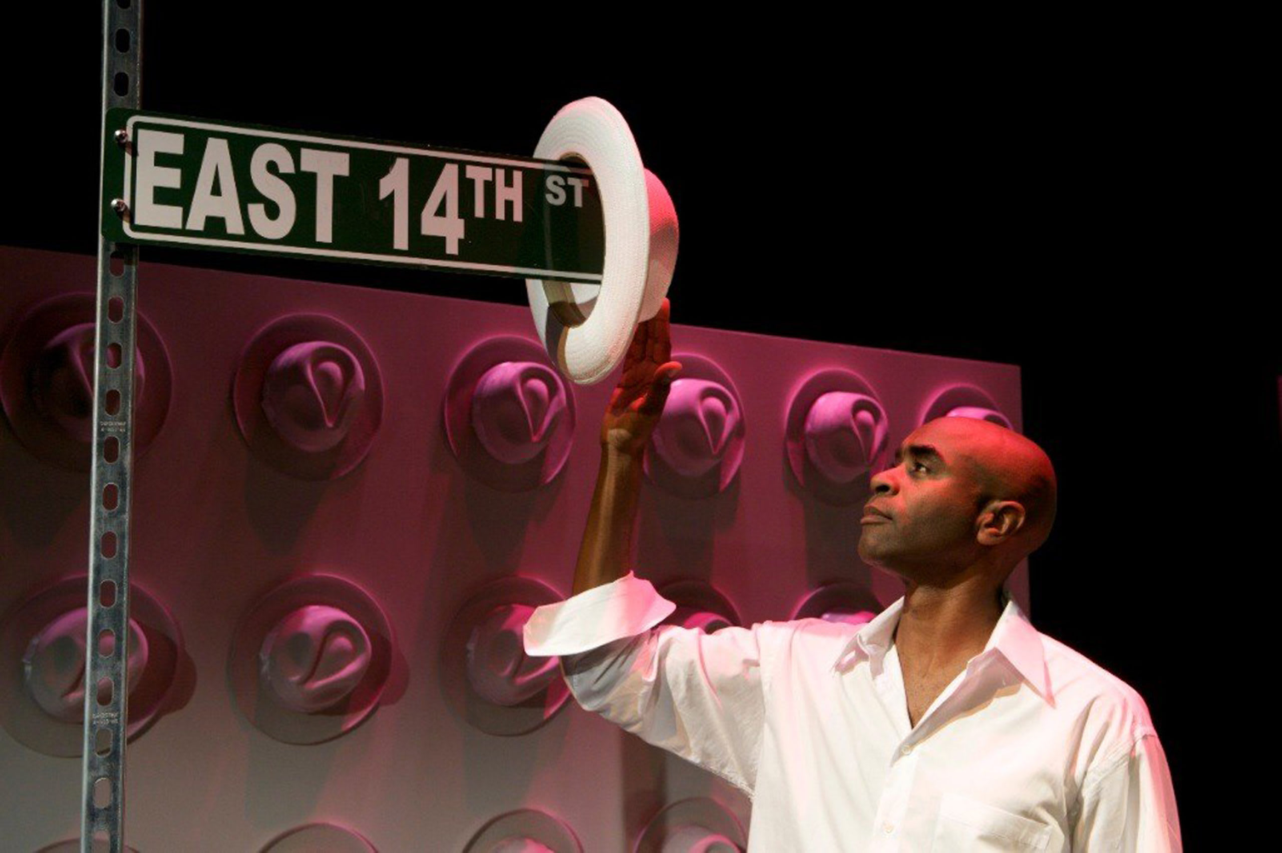 Don Reed wearing a white button-up shirt, putting hat onto East 14th street sign.