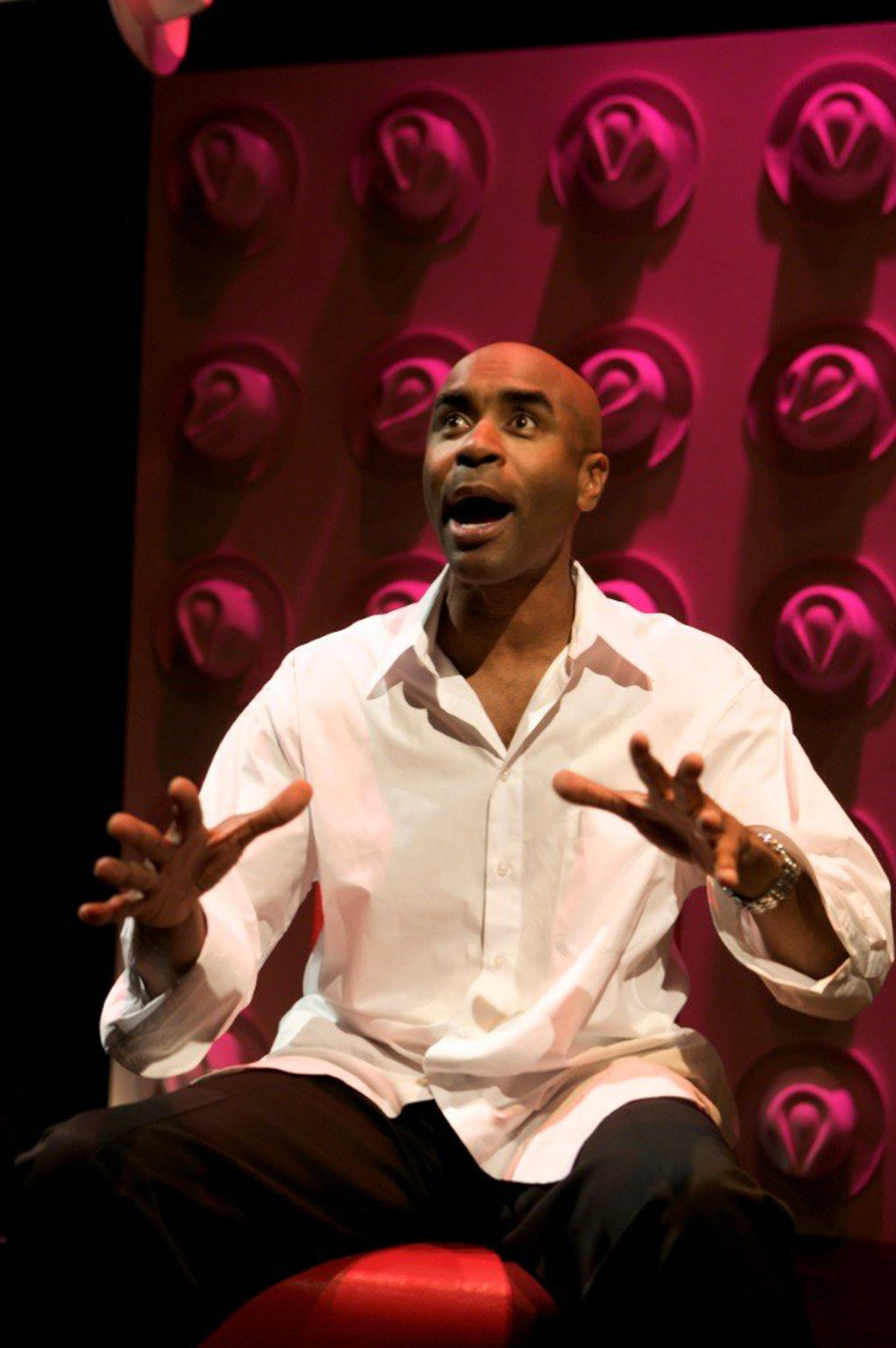 Don Reed wearing a white button-up shirt, sitting with wall of hats behind him.