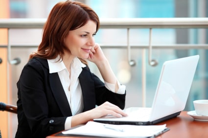 Woman in a business suit working at a desk with a laptop computer.