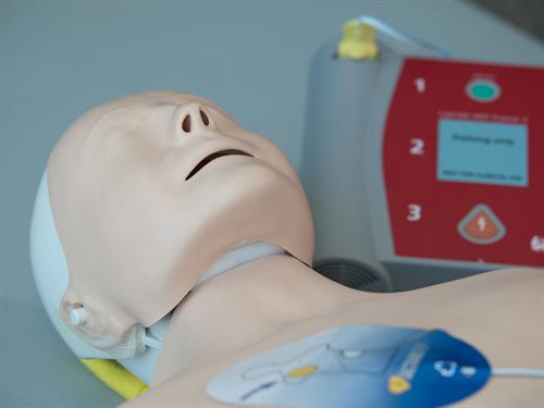 A CPR manikin with AED pads stuck to its chest and an AED in the background