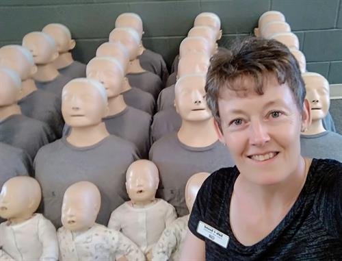 Gill McCulloch, Director, Safe + Sound First Aid Training Ltd. with Little Anne manikins wearing grey t-shirts in background.