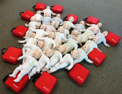 Baby CPR manikinson the ground in a heart shaped layout and surrounded by AED trainers in red cases.