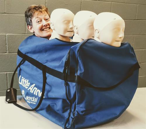 A blue bag containing 3 Little Anne CPR manikins the head of a real person sitting behind.