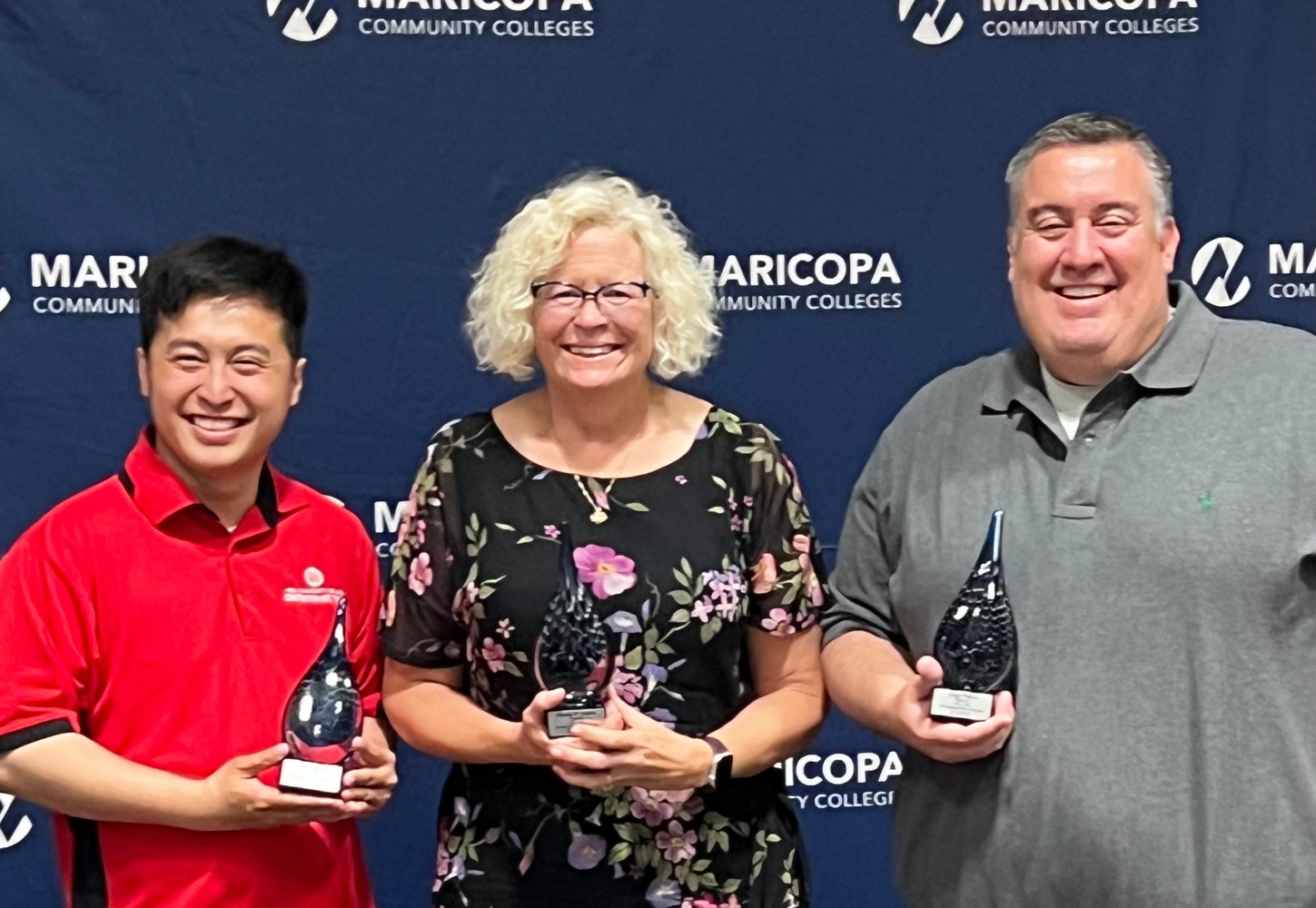 Man in red shirt smiling to the camera with a woman smiling to the camera with a man in a gray shirt
