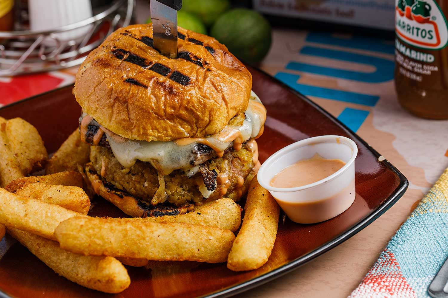 A gourmet burger with mofongo paired with fries, a specialty at Chazito's.