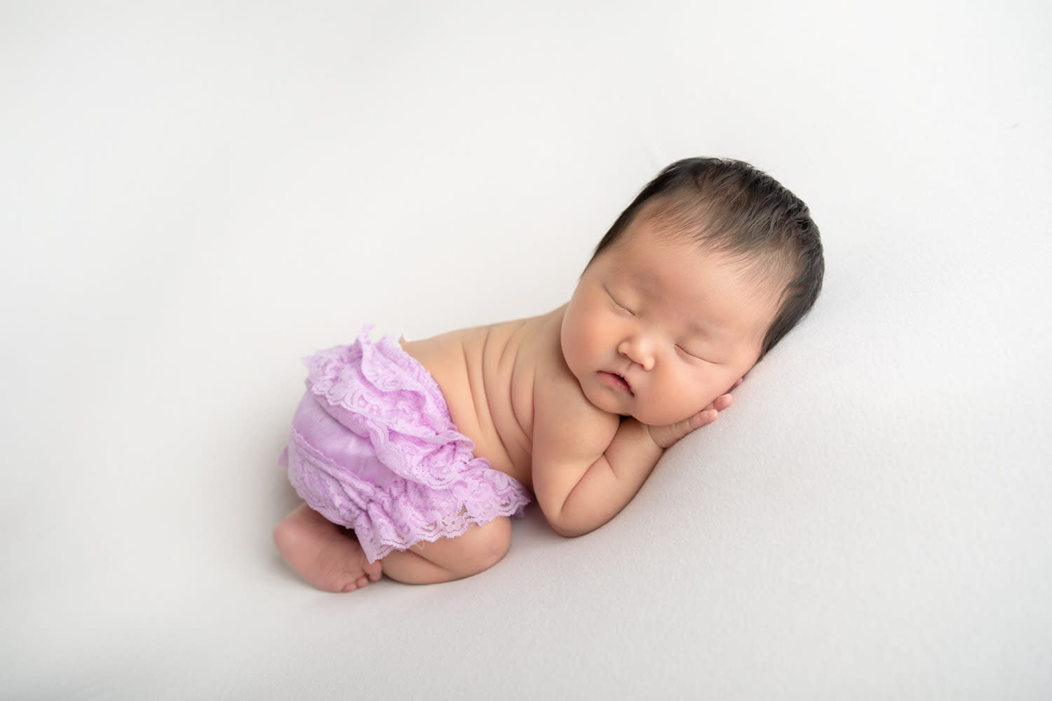 Newborn Girl cheek on hand. Lilac Diaper Cover. Sleeping