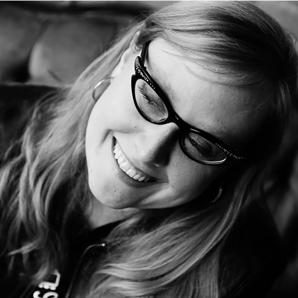 Black and white photo of a woman with medium-length blonde hair and cat's-eye glasses.