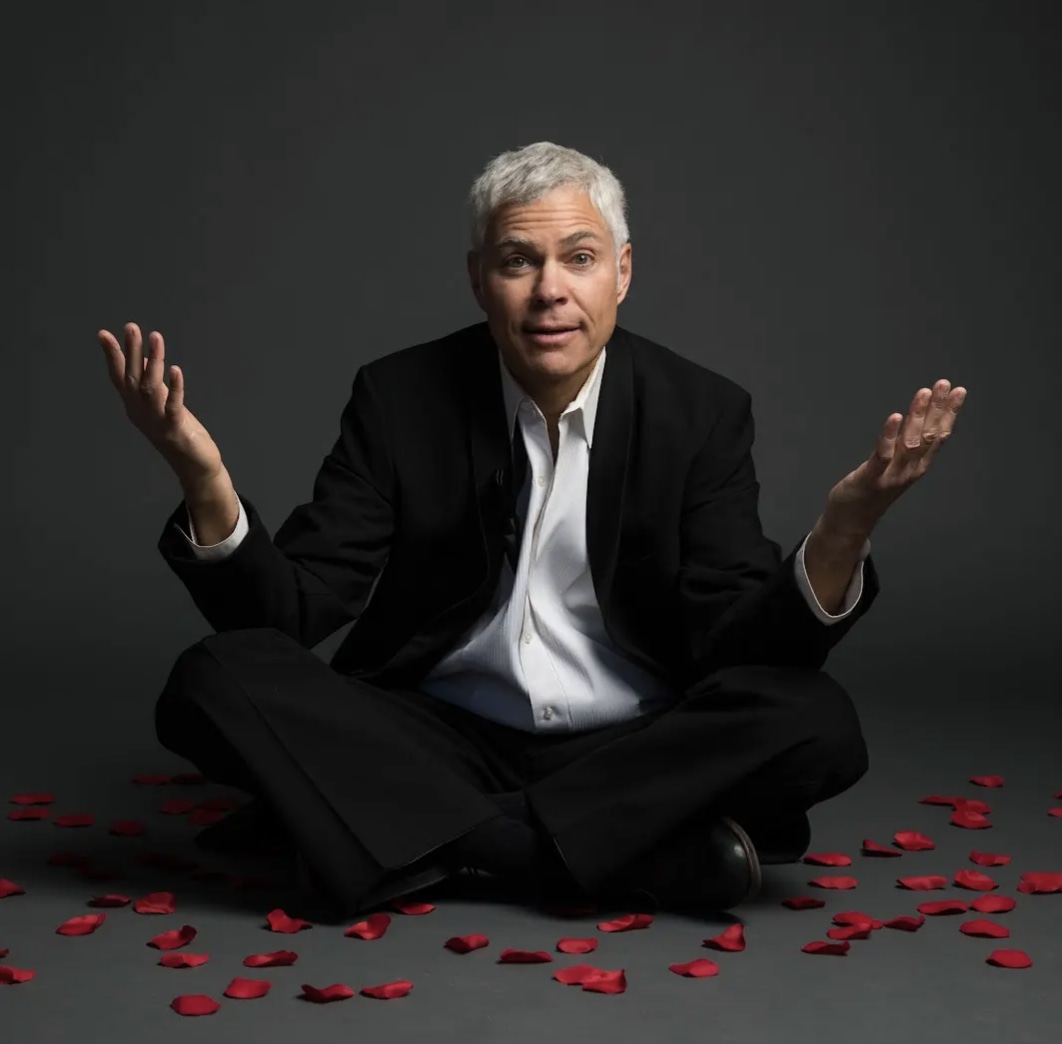 man sitting crosslegged in a suite over scattered rose pettles