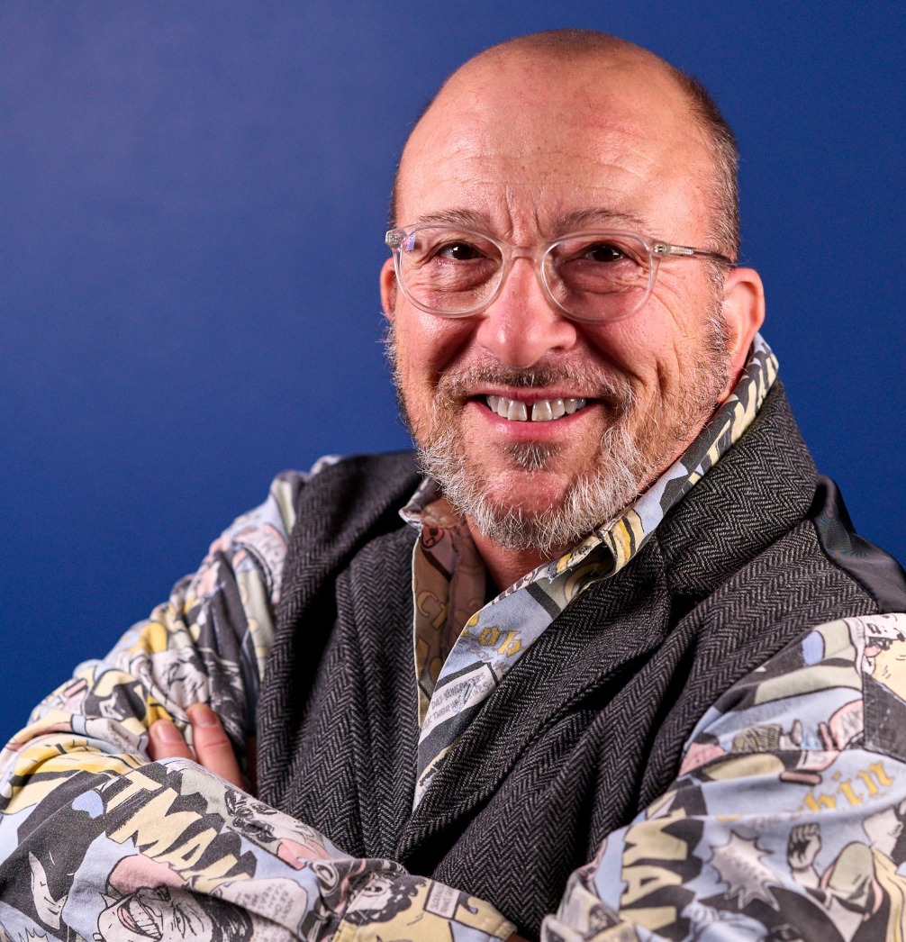 portrait photo of Mitchell Hunter. Smiling, arms crossed, grey vest over superhero comic shirt