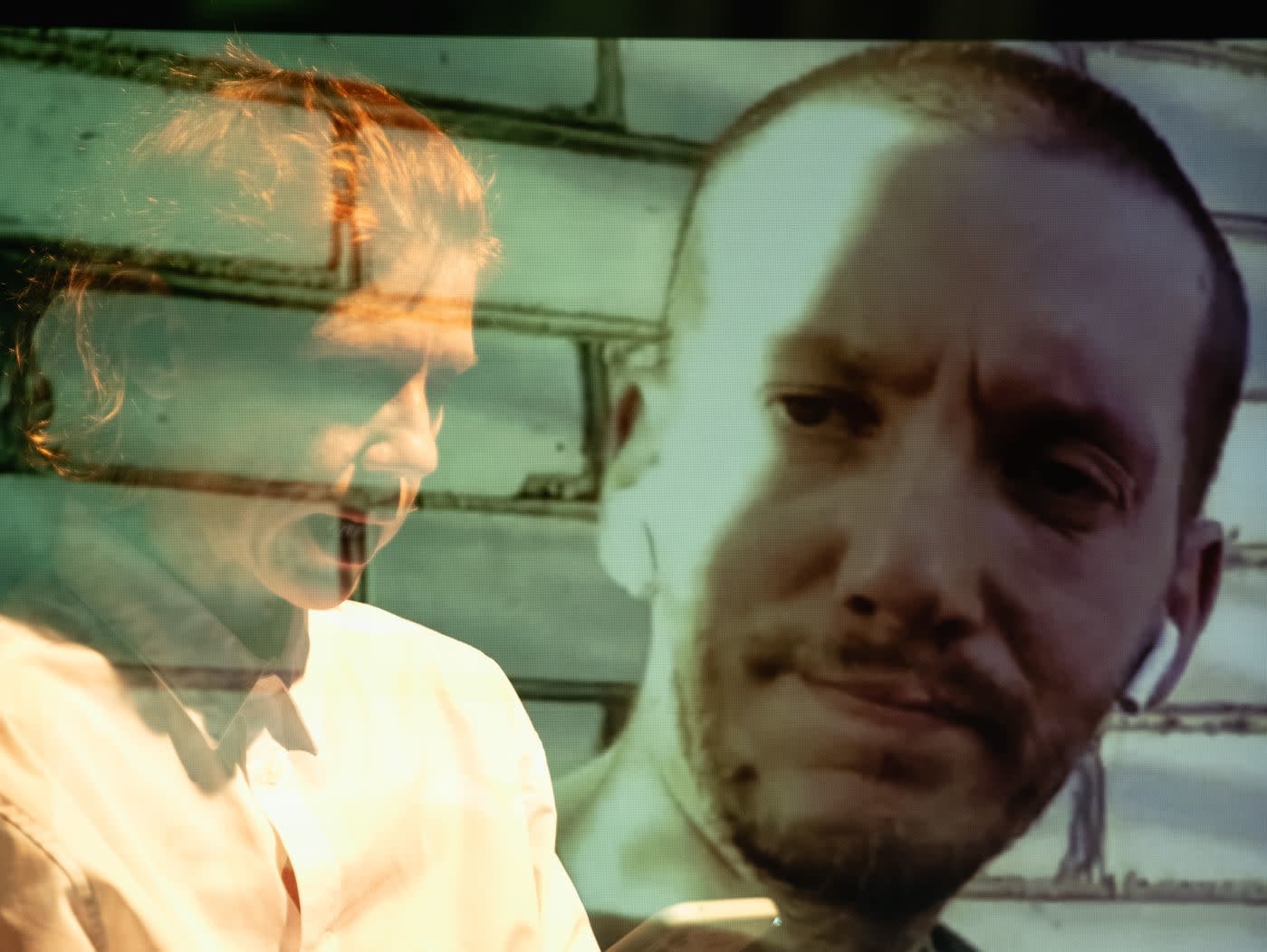 The faces of two men are seen, one a ghostly silhouette in a white dress shirt, the other in high-contrast, wearing airpods