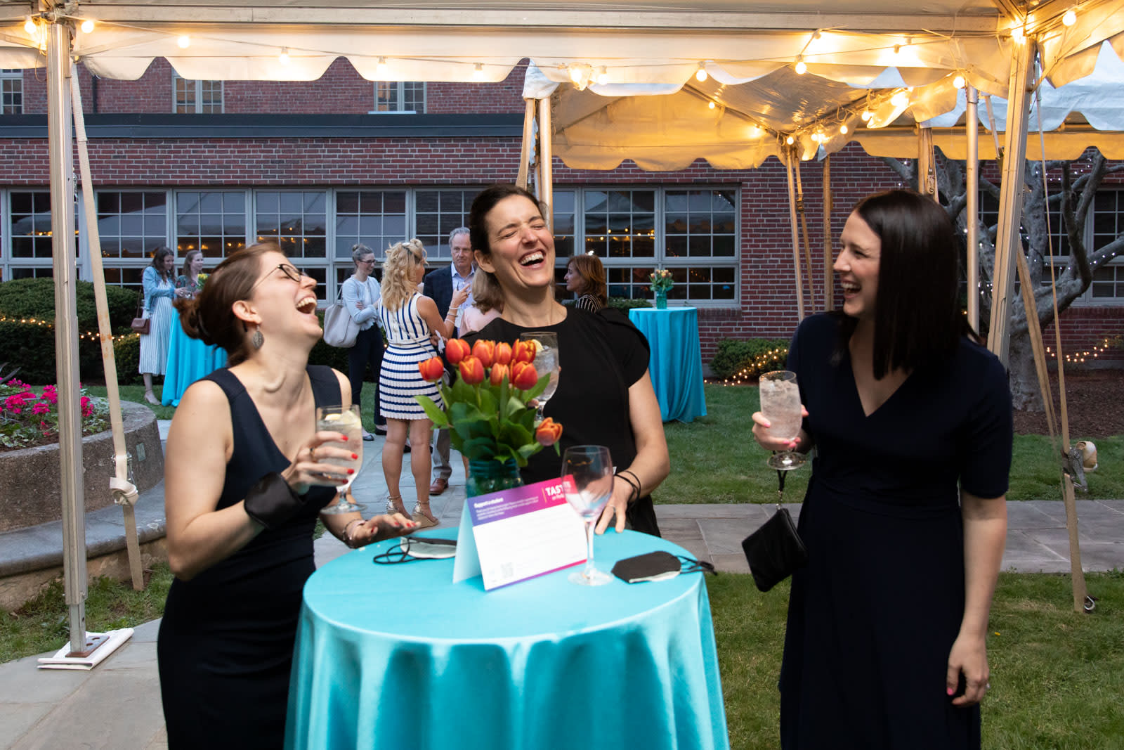 3 woman laugh around a table in a tented outdoor courtyard