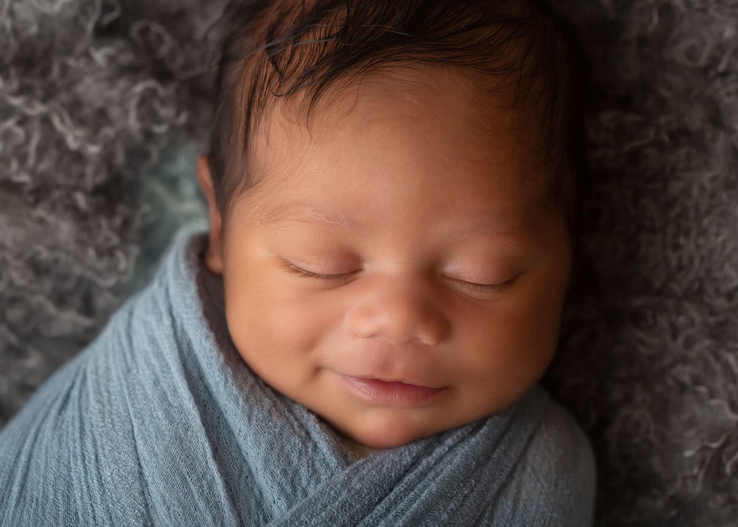 Newborn Boy Portrait wrapped in blue. Smiling