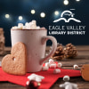 A cup of hot chocolate and heart shaped gingerbread cookies with the Eagle Valley Library District logo.