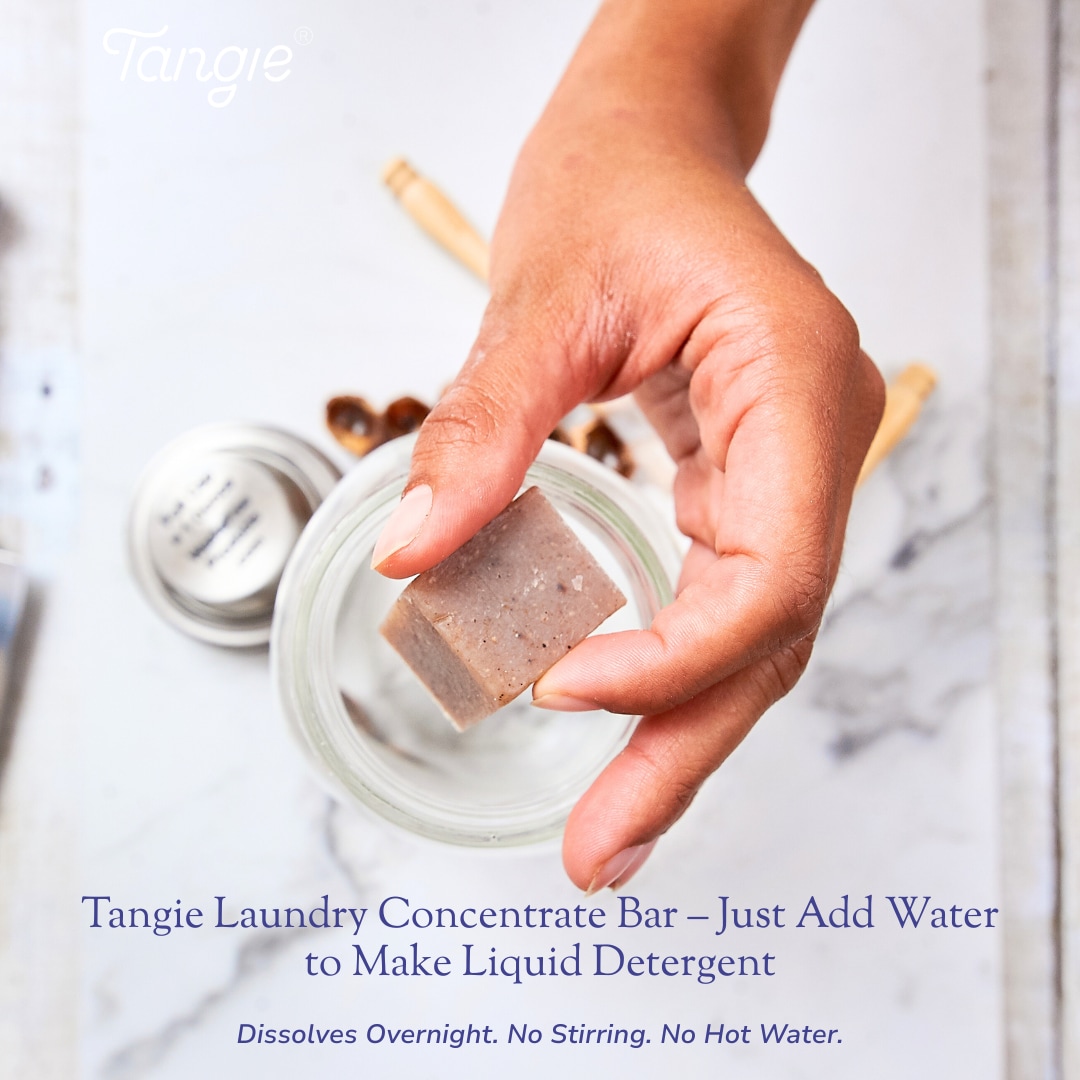 Hand drops a Tangie Laundry Concentrate Bar into a glass jar of water to dissolve into liquid detergent.