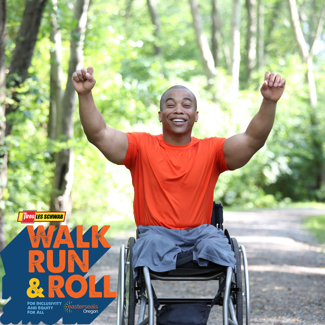 Man in wheelchair, wearing an orange shirt and gray shorts. He has his arms up in the air to celebrate, smiling.