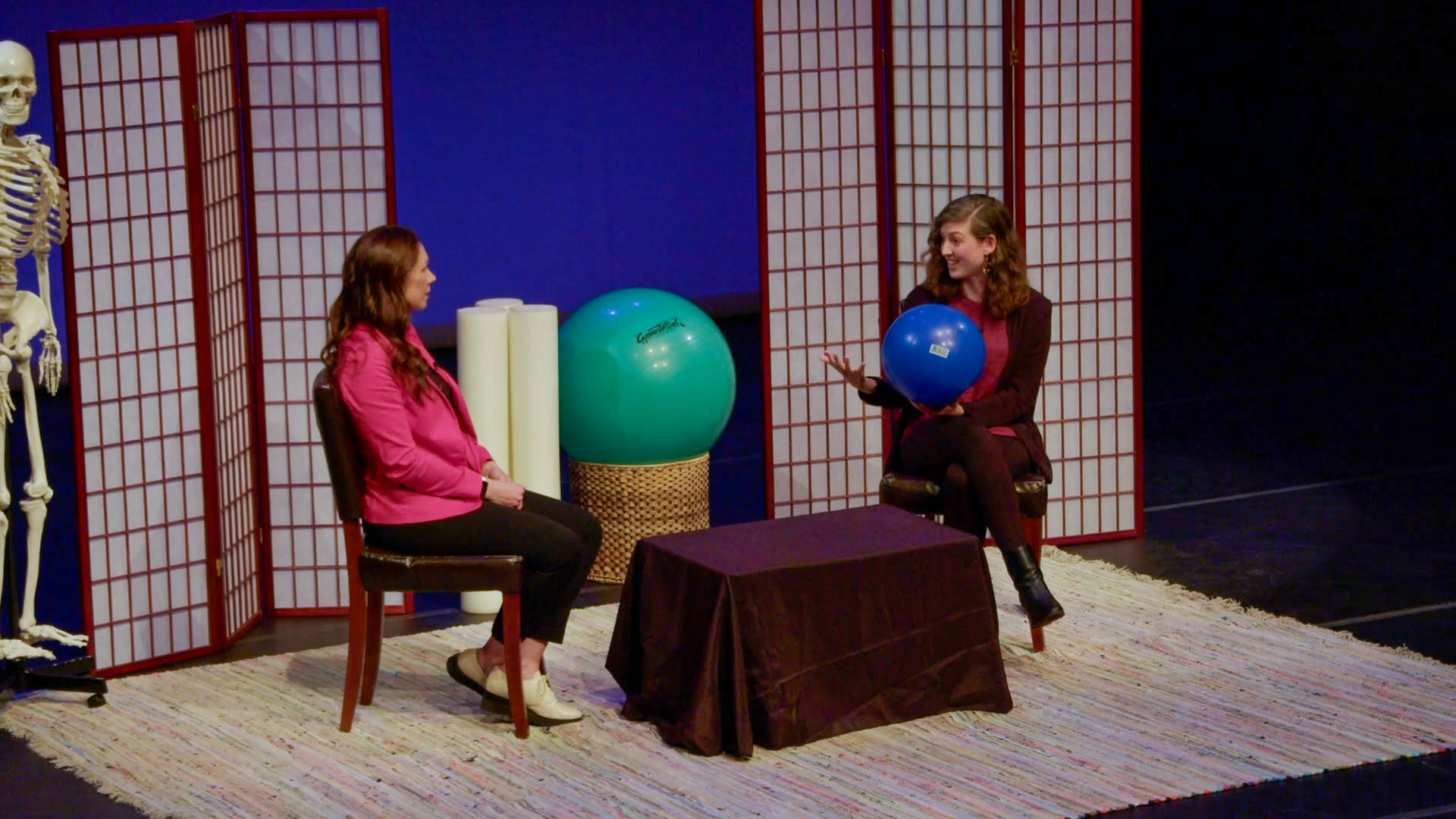 Two persons sitting on stage and actively participating in a conversation.