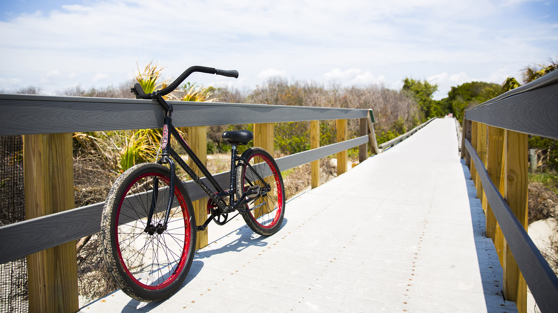 A black bicycle leaning against a railing on a path crossing sand dunes on Jekyll Island.