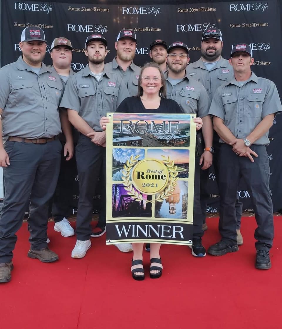 A group photo of the Matthews Lighting & Electric team standing on a red carpet. A woman in the center is holding a "Best of