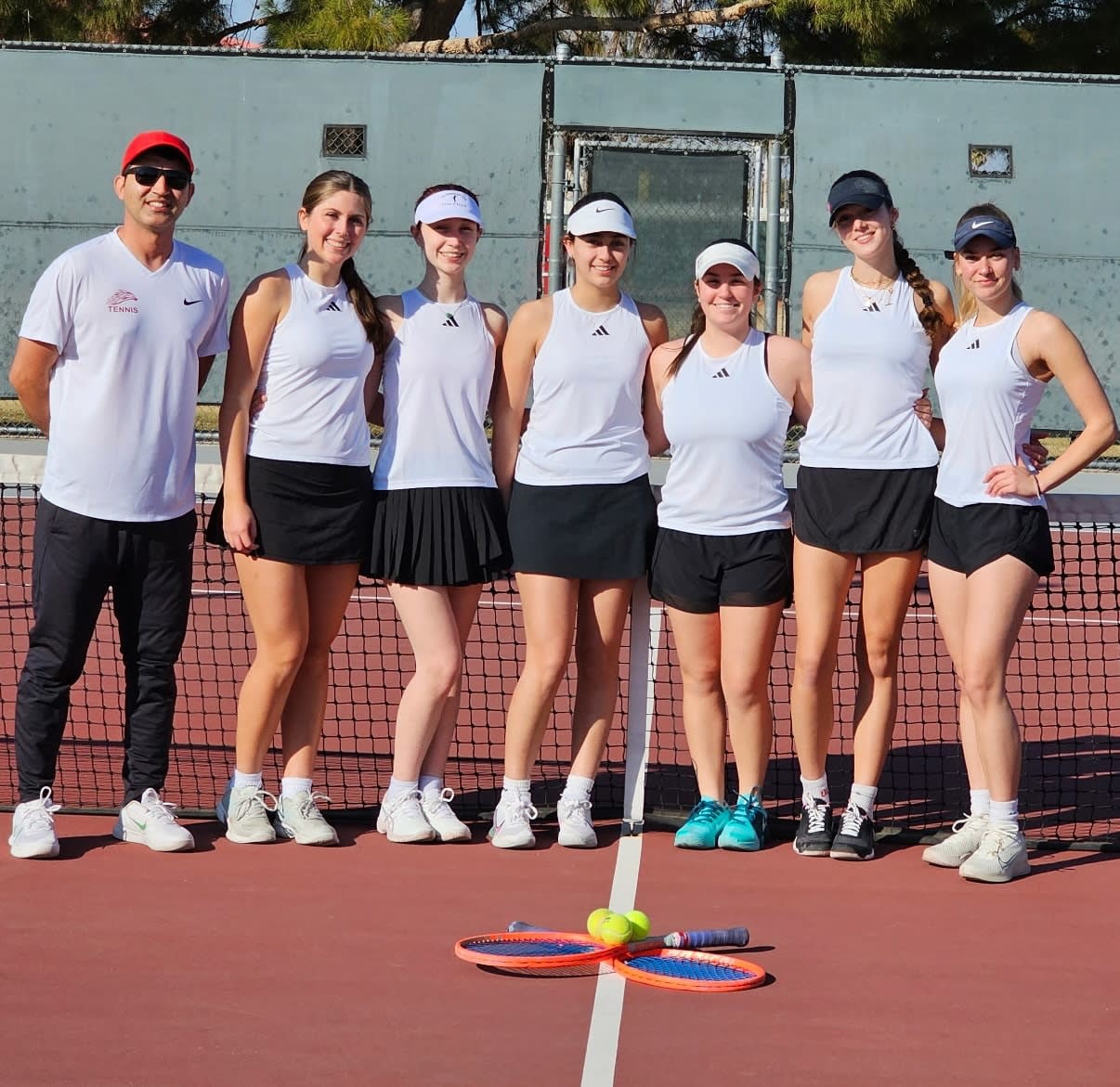 MCC Women's tennis coach and team of six lined up in front of a tennis net.