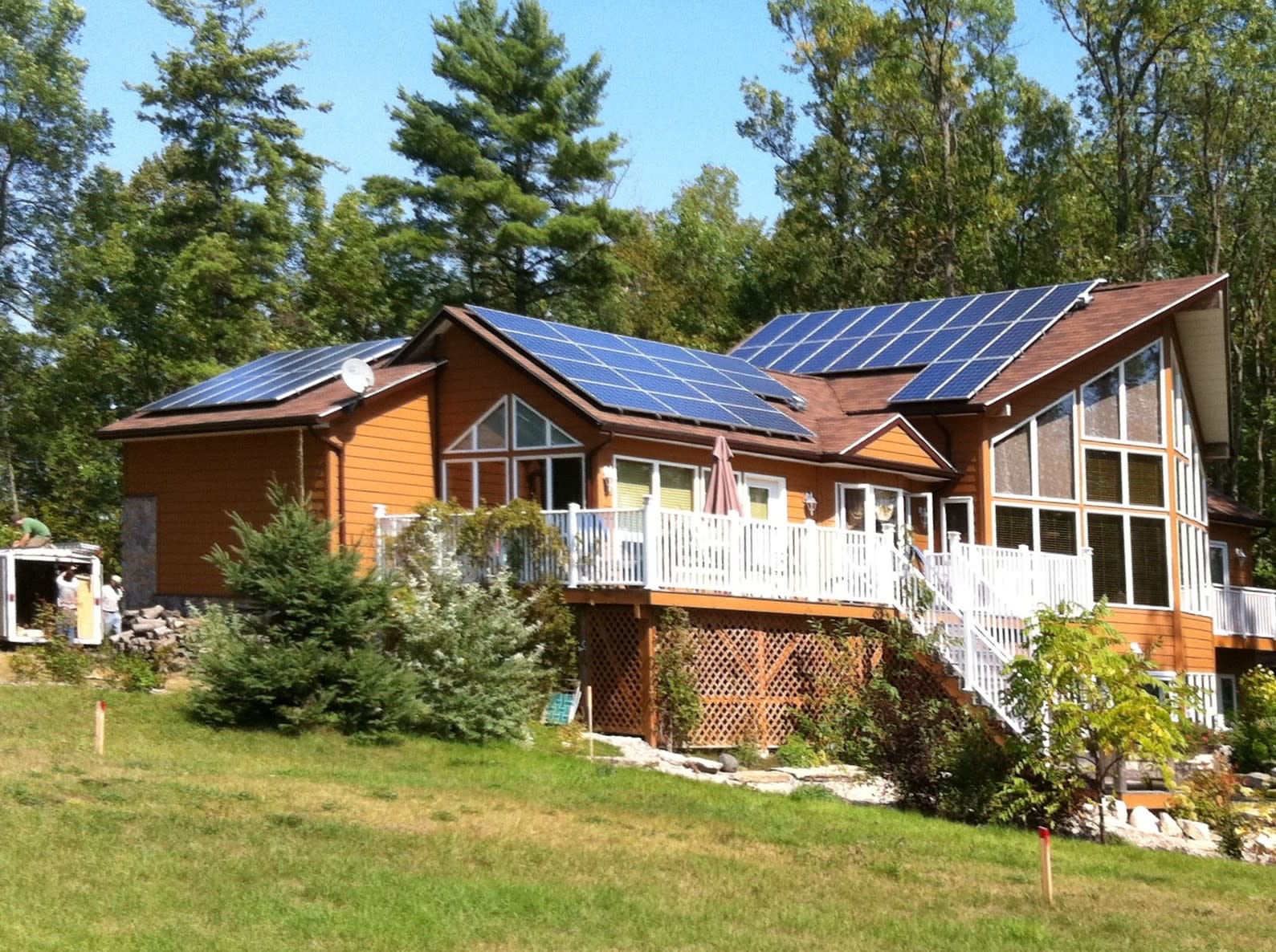 Brown sided home with blue solar panels on the rooftop. Green trees and blue sky!
