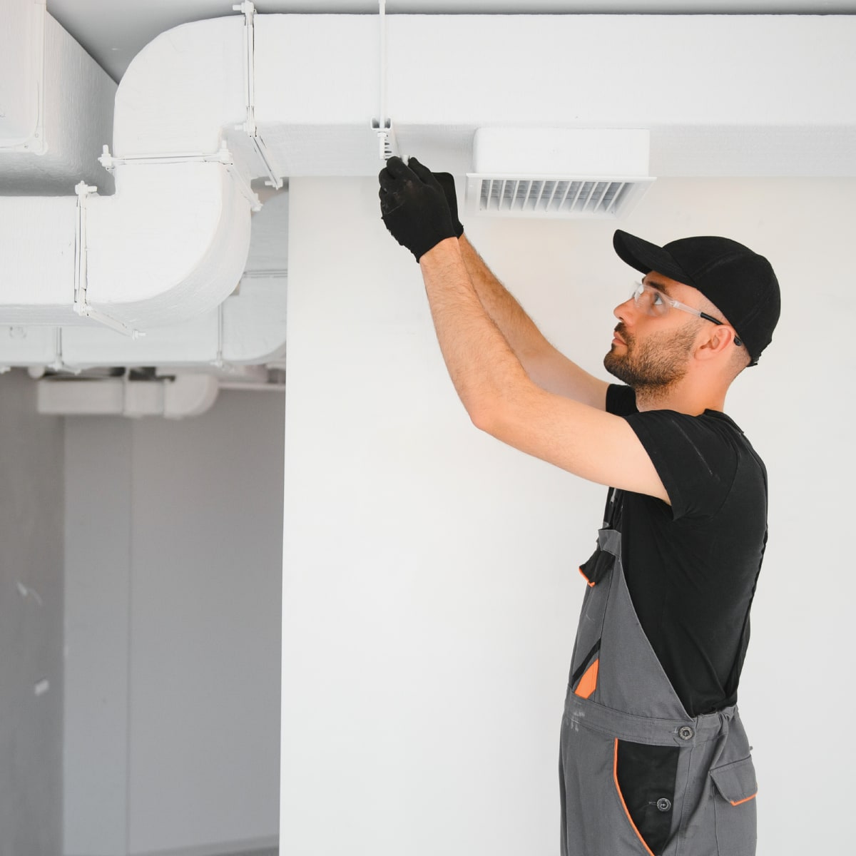HVAC service technician in gray overalls installing ductwork