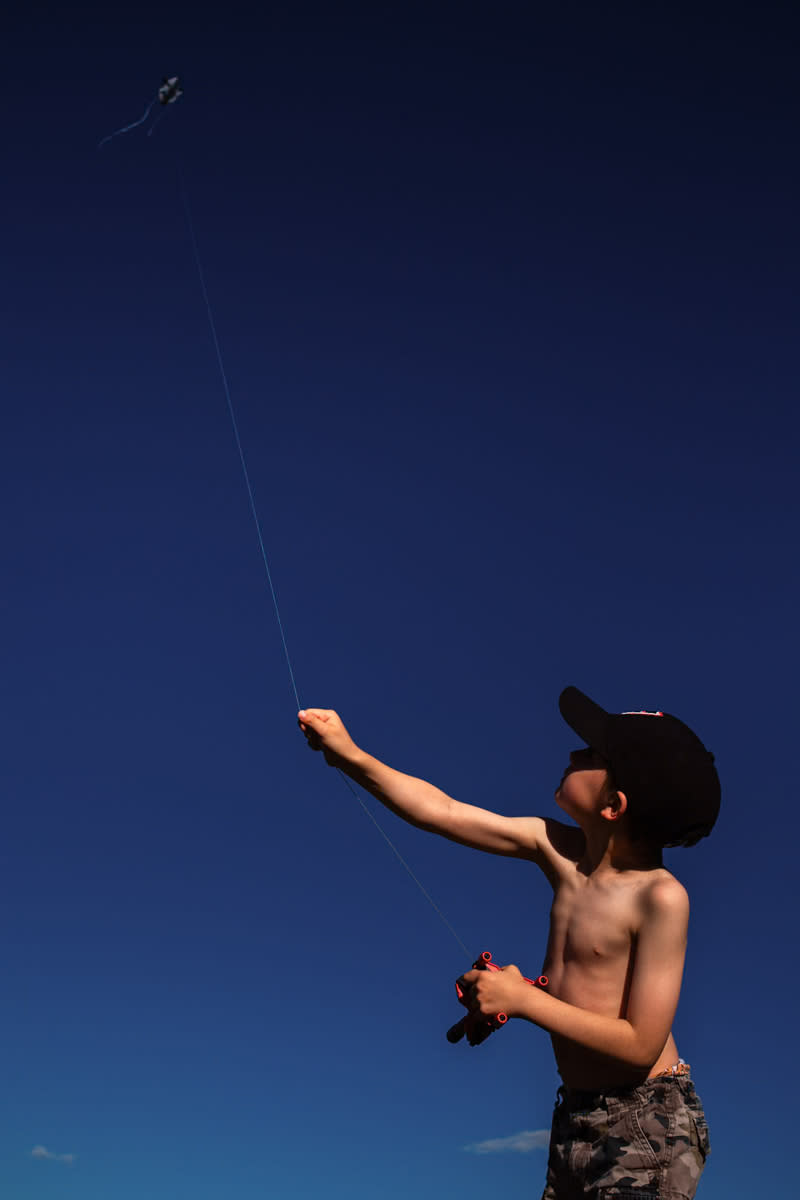 young boy flies a kite into a big blue sky