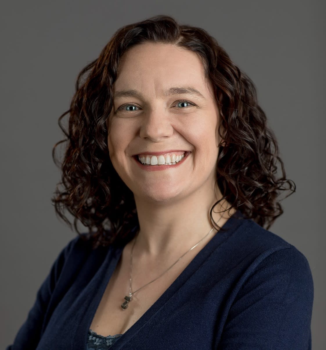 Picture of a smiling female-presenting person wearing a navy blue sweater with their arms crossed.