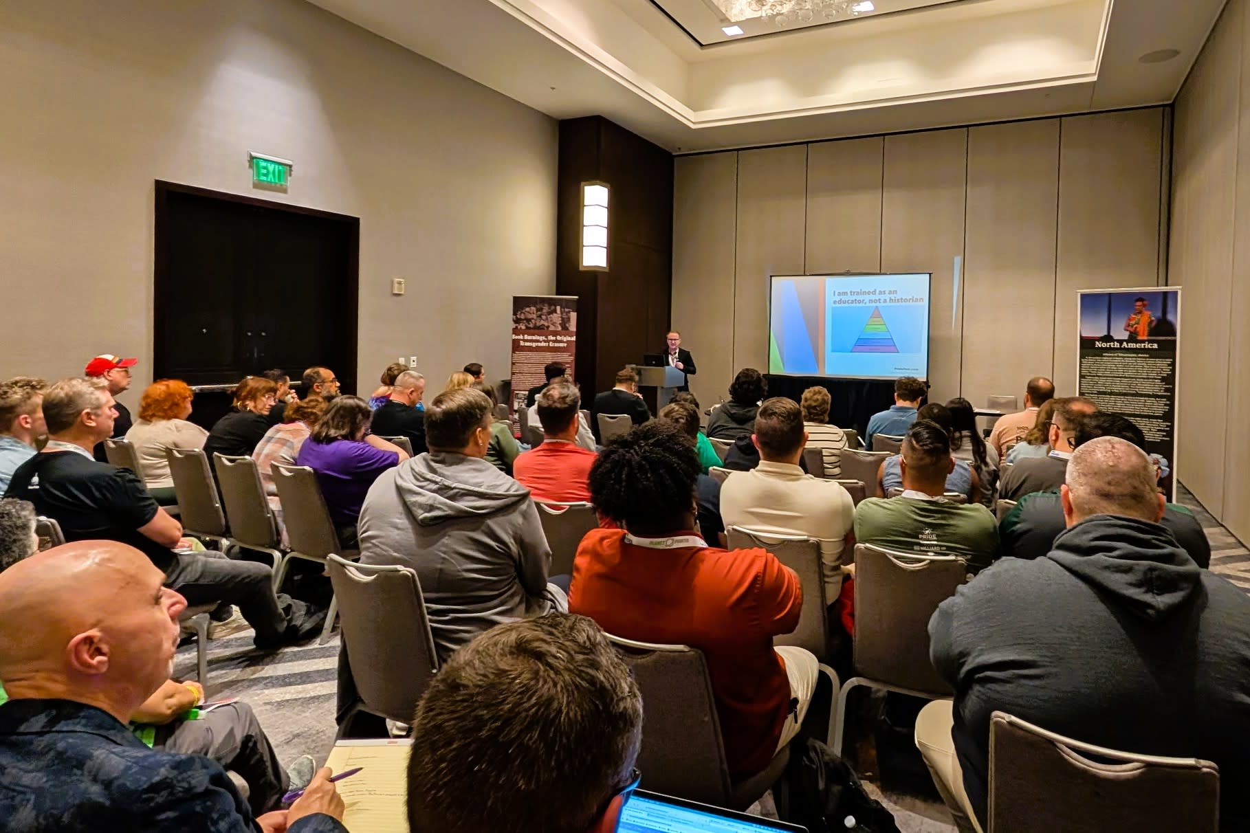 A crowded meeting room with Vince standing at the front in front of a projector screen