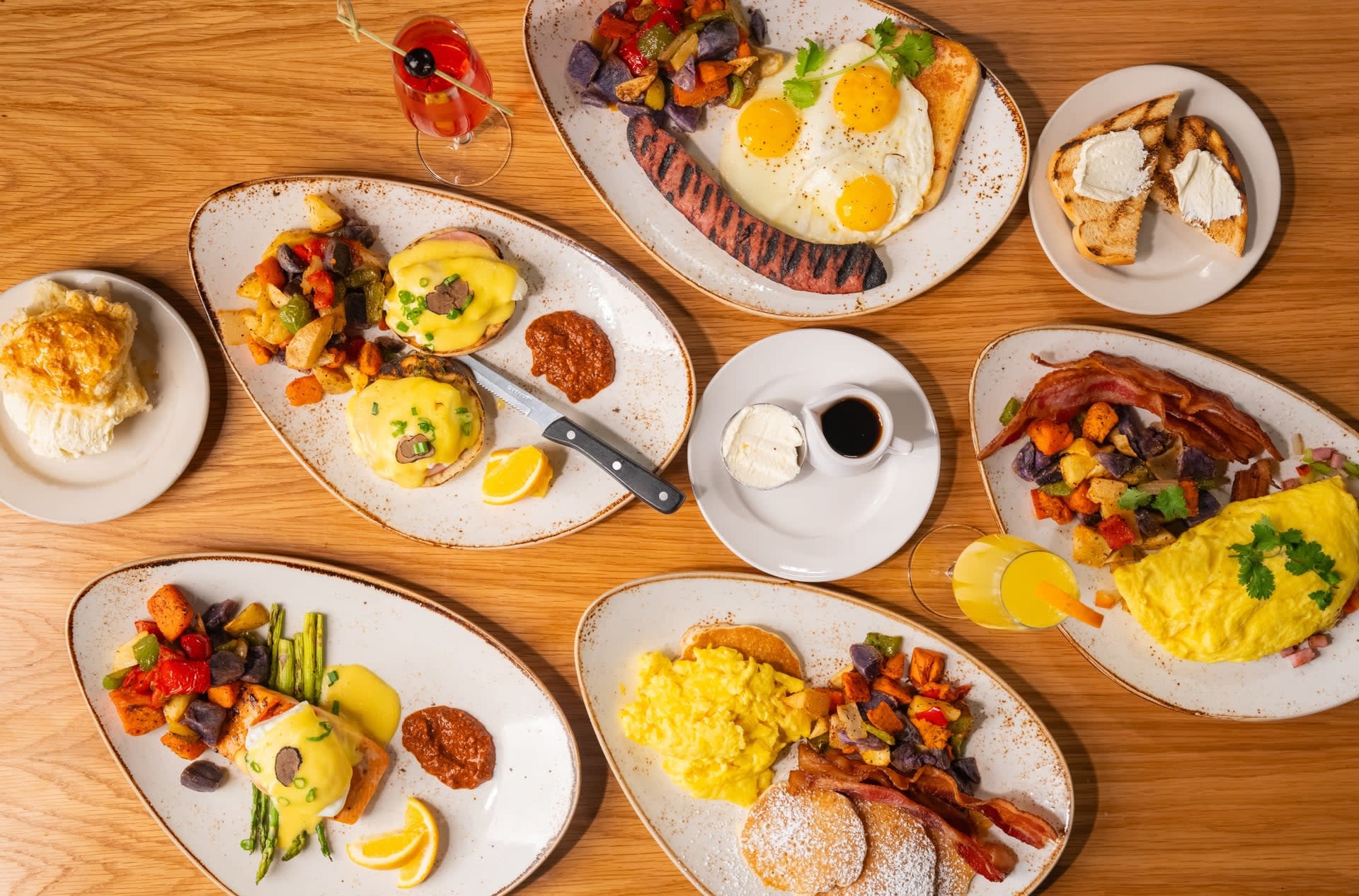 Assorted brunch plates at Rascal Modern Diner including eggs Benedict, omelets, pancakes, breakfast sausage, roasted potatoes