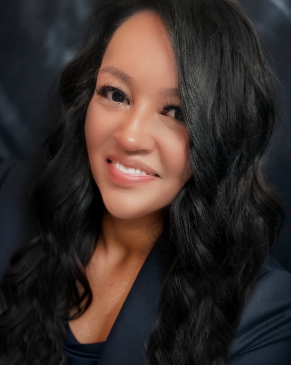 picture of latina with black hair and smiling looking at the camera dressed in a deep navy blue suit