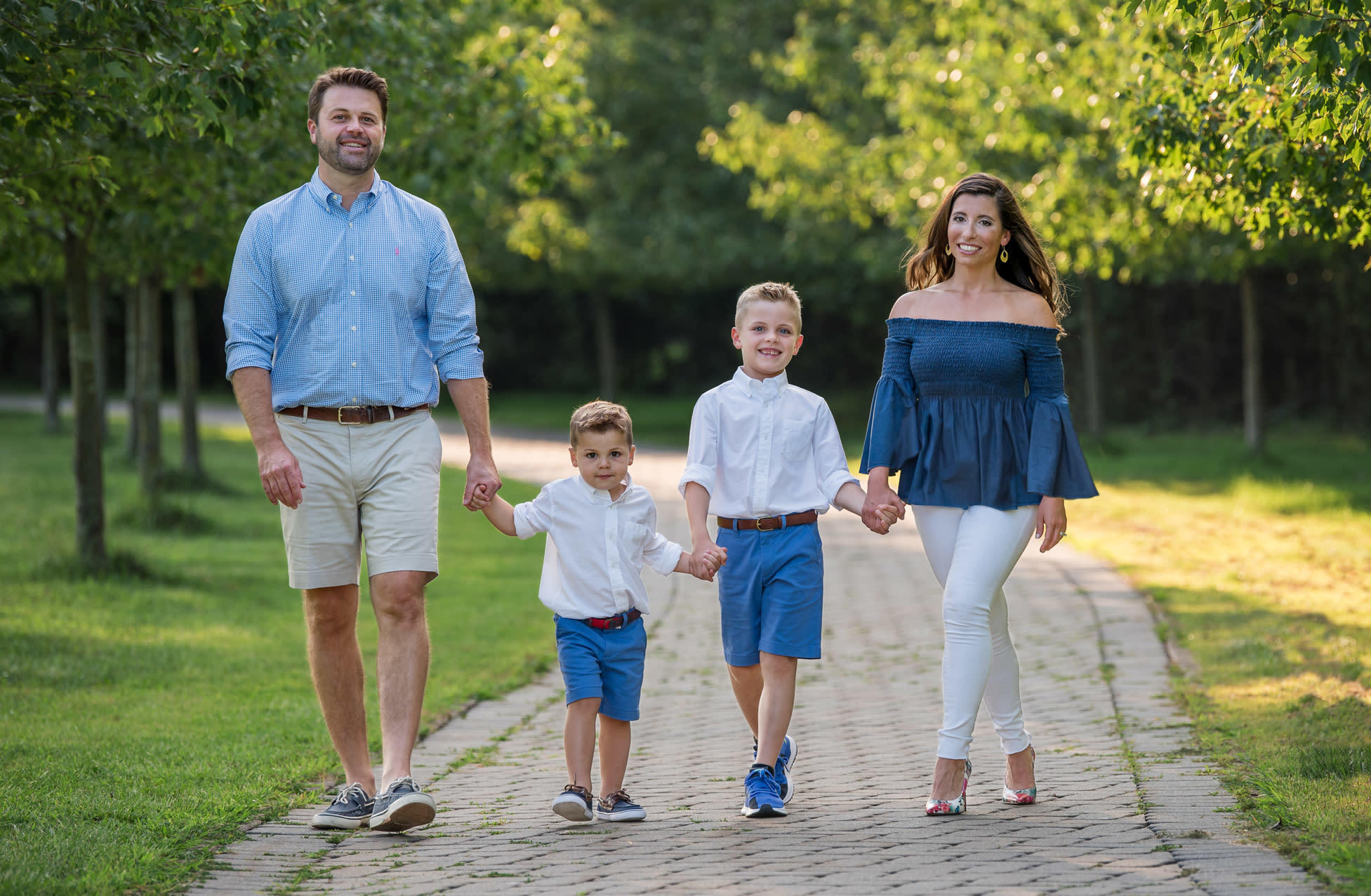 A Caucasian family of 4 walking together hand in hand at a park.