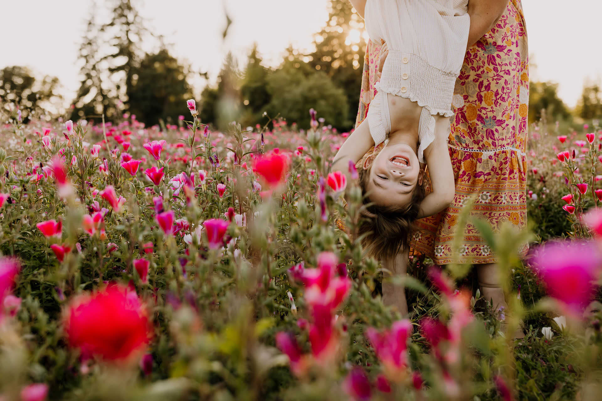 wildflower field of pink flowers with a little girl laughing while hanging upside down