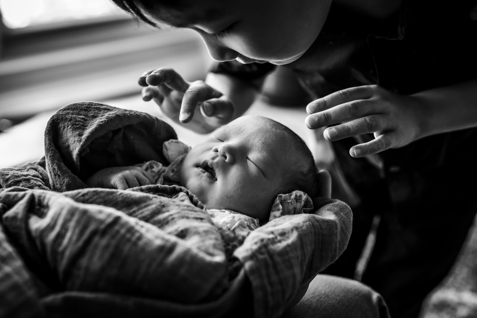 boy looking over his swaddled newborn sister