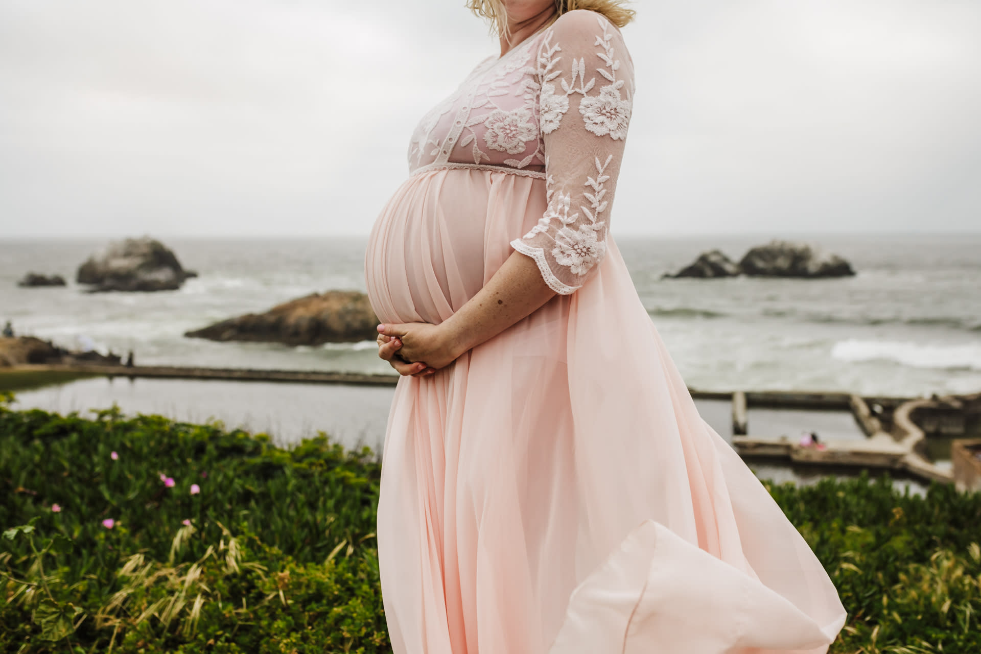 baby bump with mom's pink dress blowing in the wind above the ocean