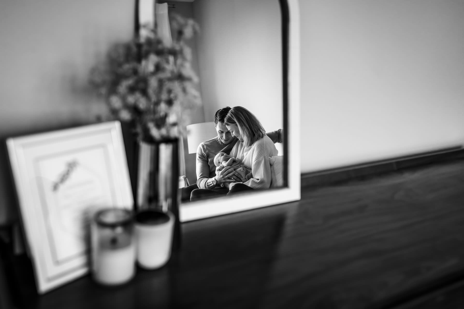 reflection in a mirror of parents holding newborn baby while sitting on bed