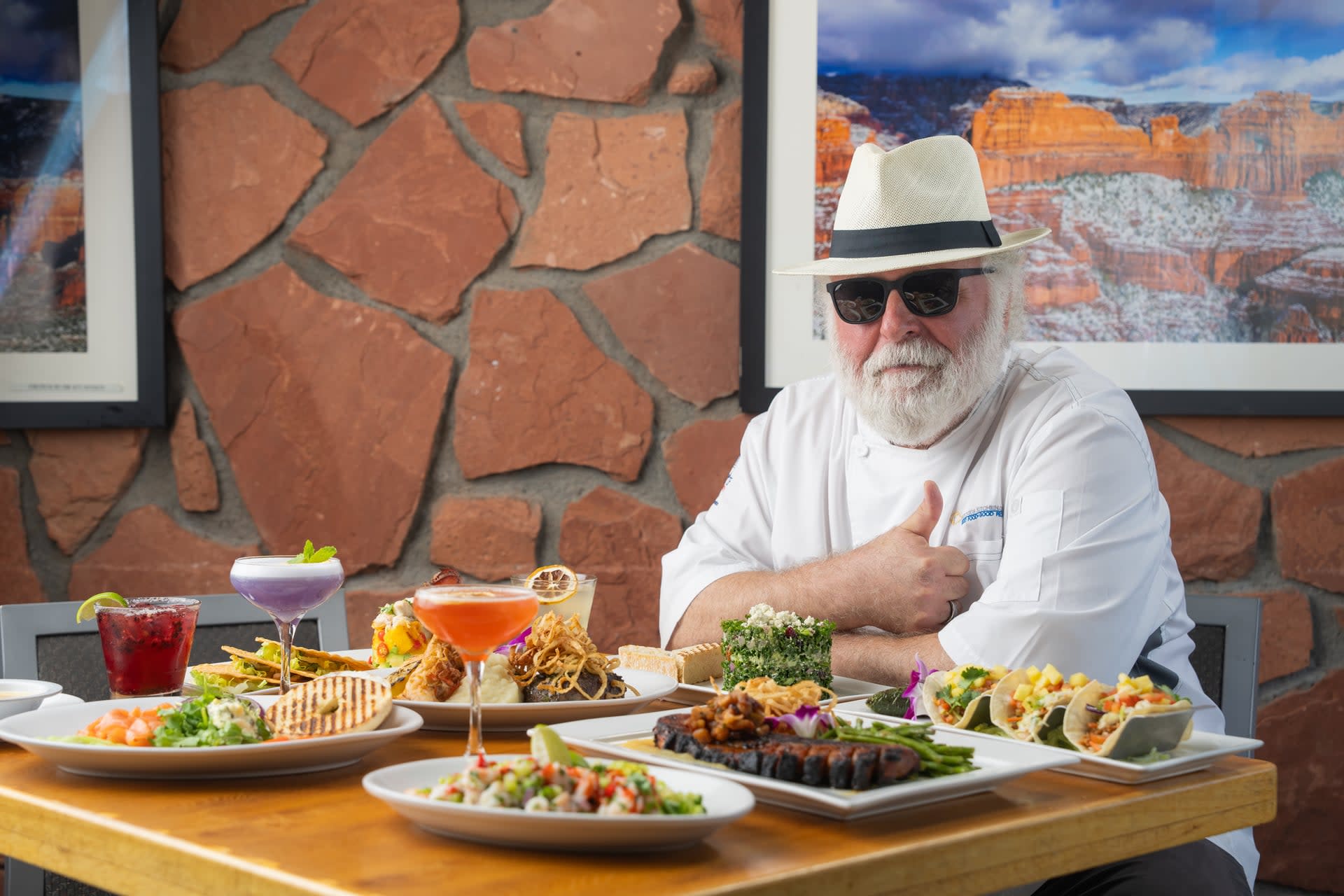 Chef Mercer Mohr seated at a table with an assortment of Mesa Grill Sedona Airport dishes and cocktails in front of him.
