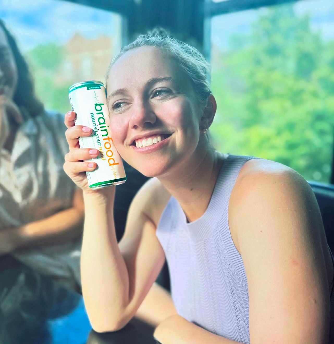 Woman smiling while drinking Watermelon Fizz Brainfood — caffeine-free functional sparkling water for focus, energy, + stress