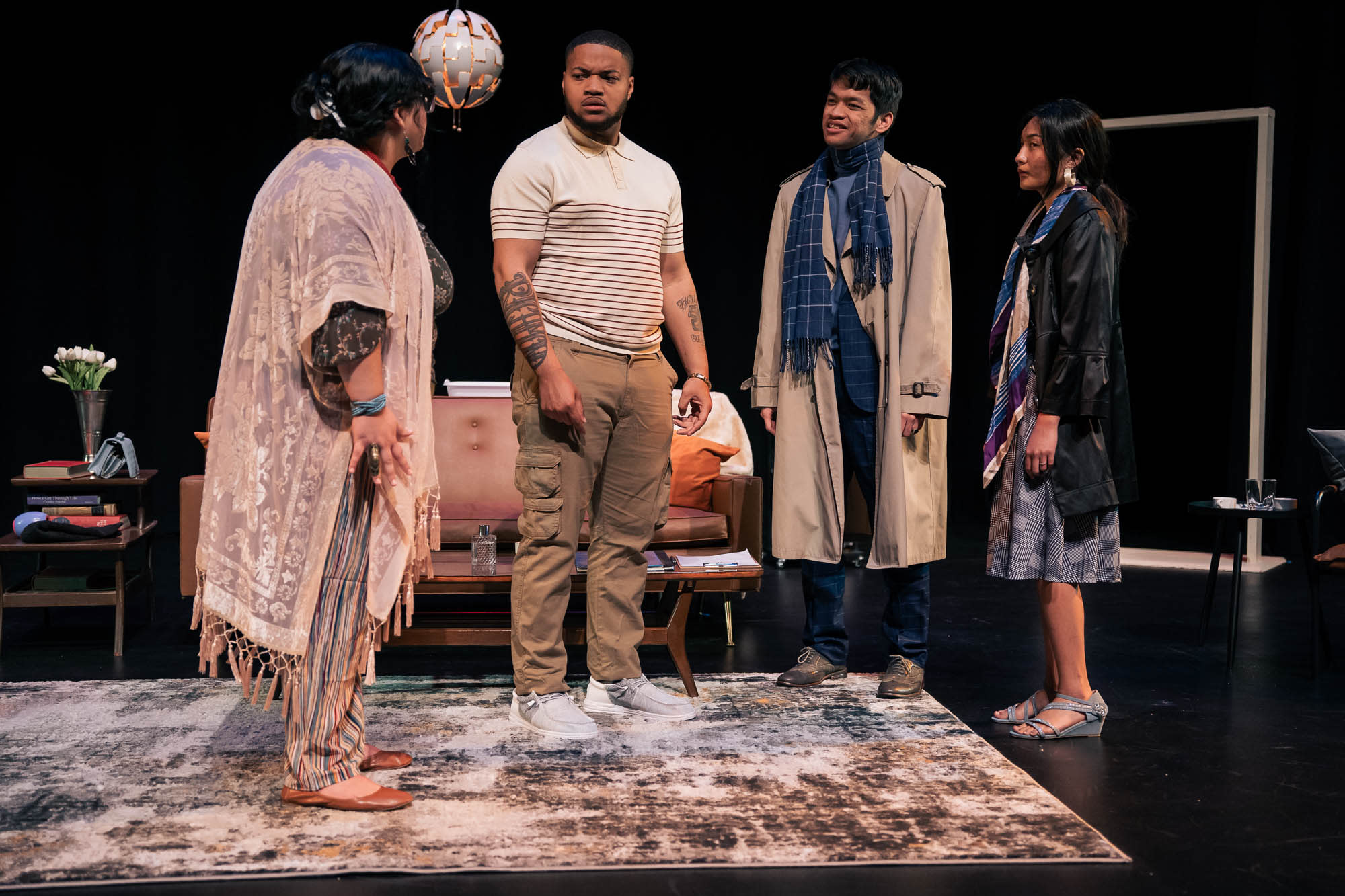 Two men and two women stand in a semi circle arguing. The woman closest to the camera is turned toward the other