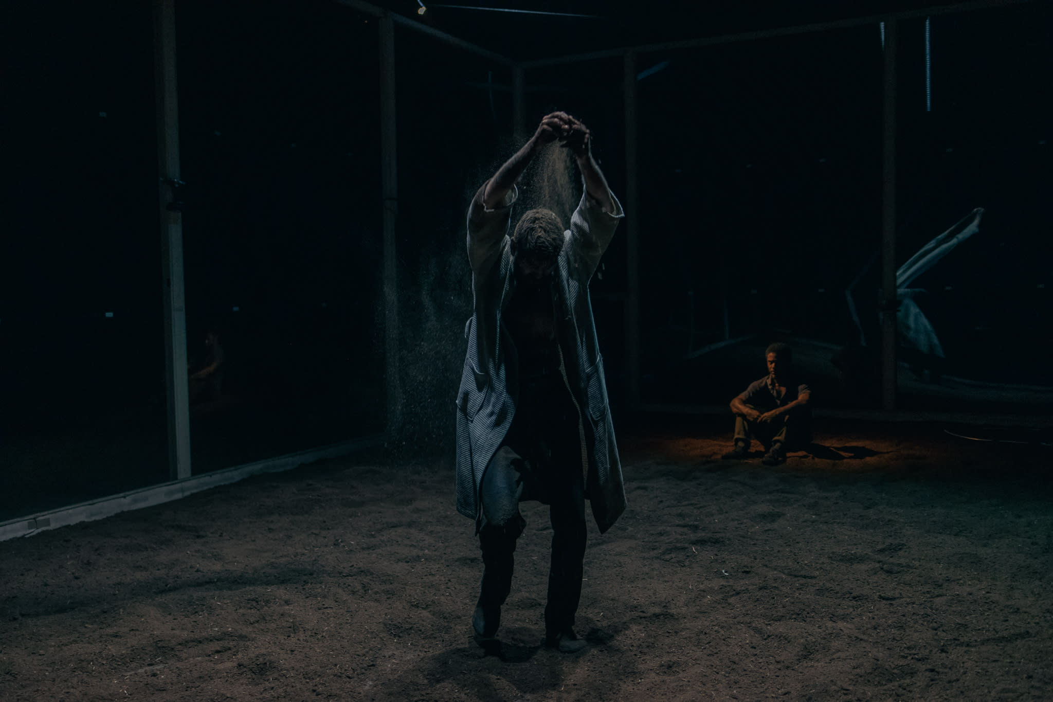 Dancer sprinkles dirt from fingers in the middle of the room