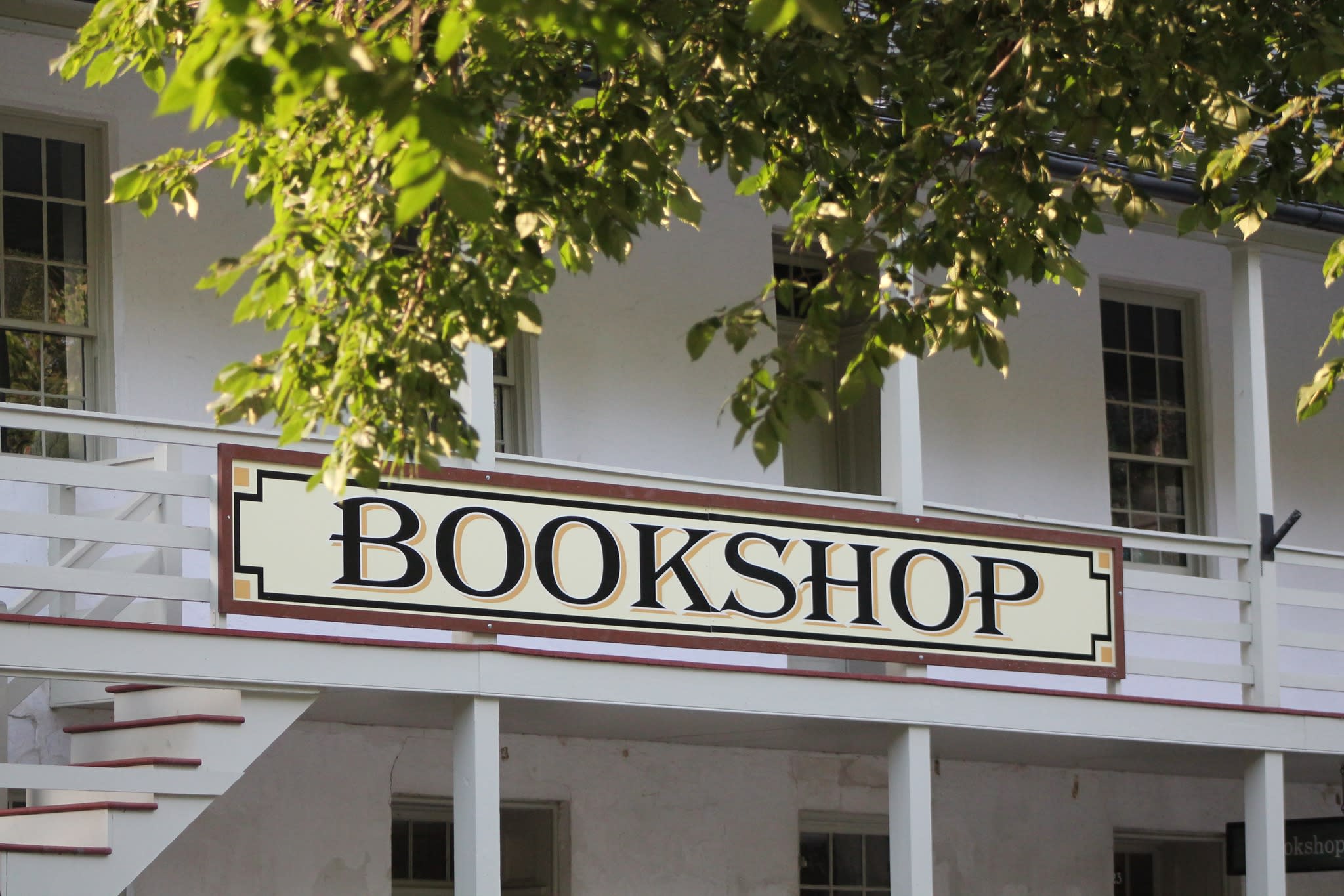 The second balcony of the Park Bookshop with sign reading “BOOKSHOP,” partially shaded by green tree branches.