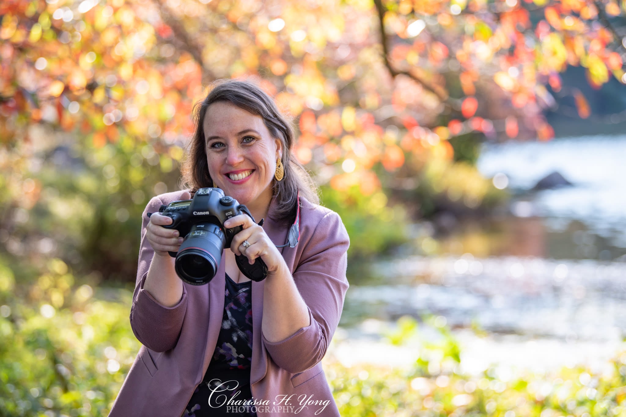 A woman holding a DSLR camera at a park during Fall season.