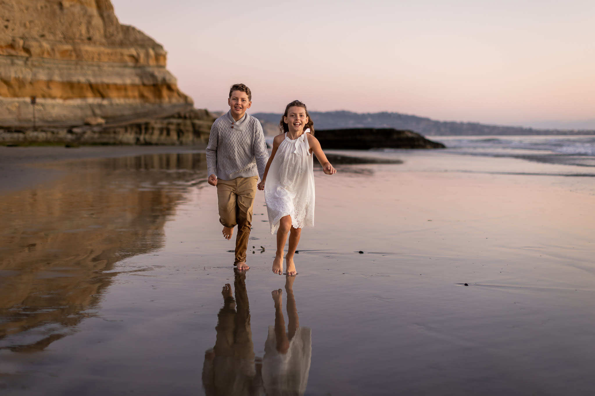 young siblings running on beach