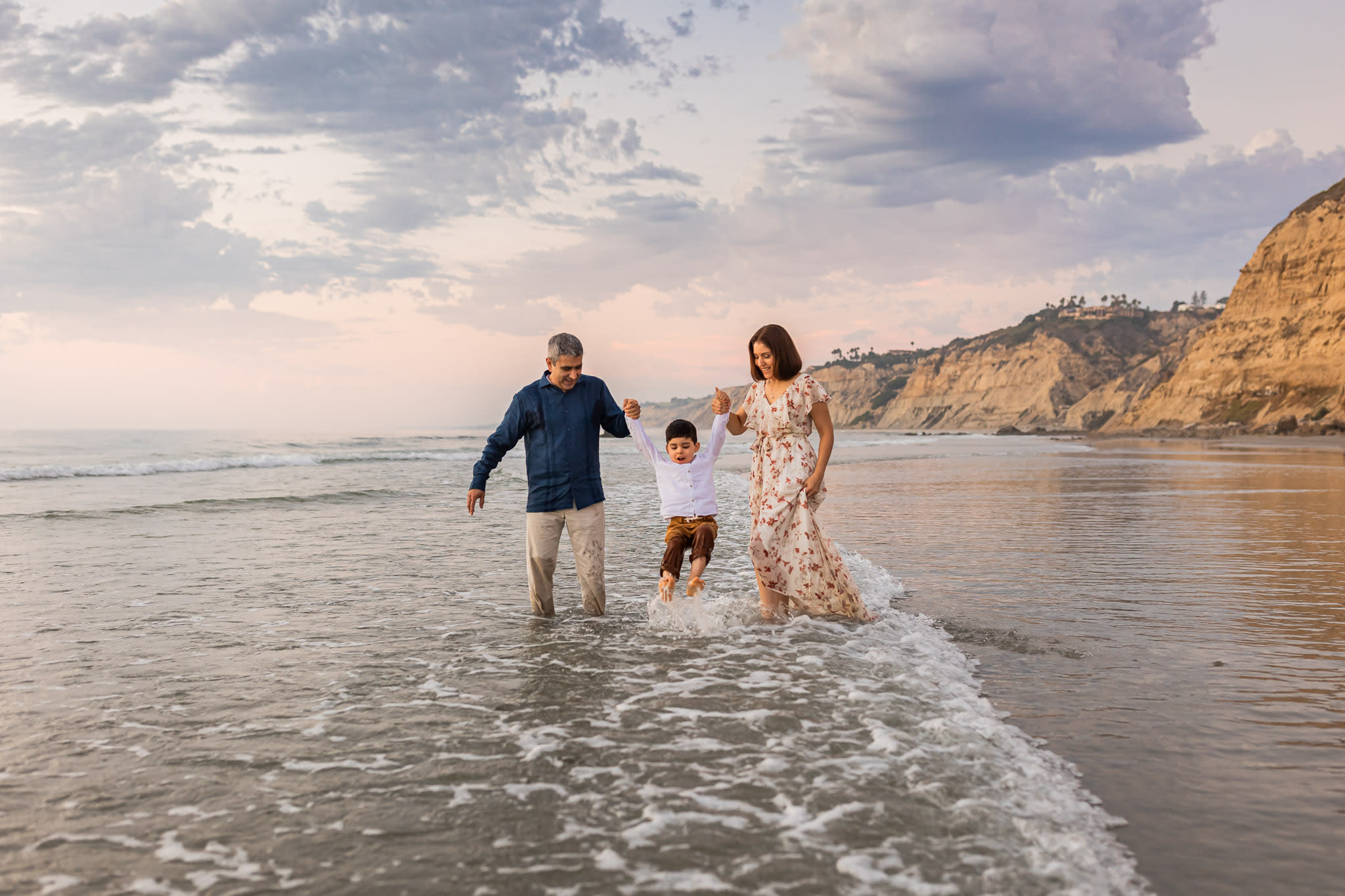 Parents swinging toddler son above wave